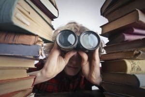 anonymous-person-with-binoculars-looking-through-stacked books