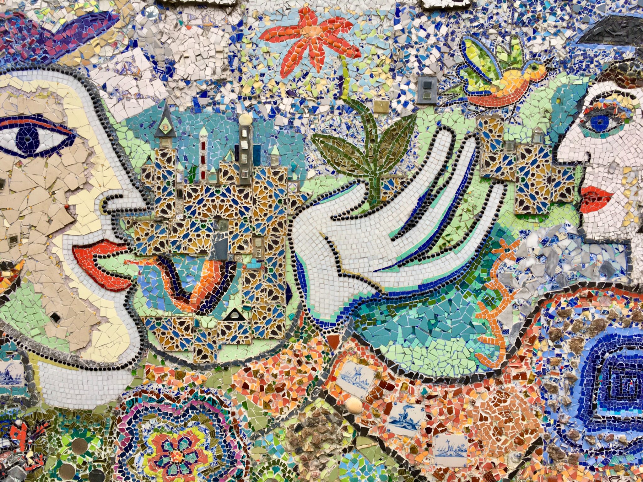 Multicoloured mosaic with two faces looking at each other with hands outstretched.