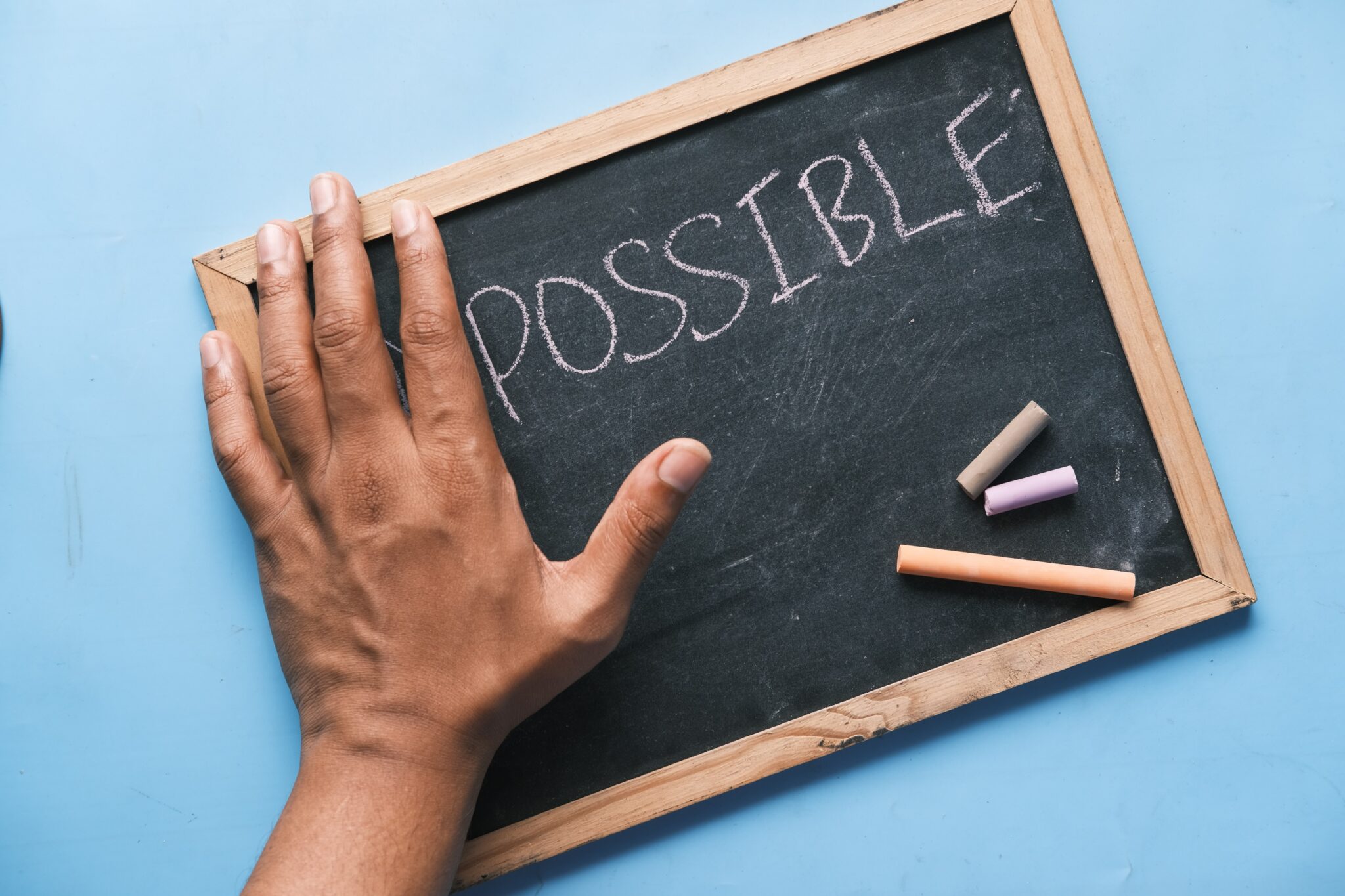 Hand holding a chalk board that reads the word, 'POSSIBLE'.